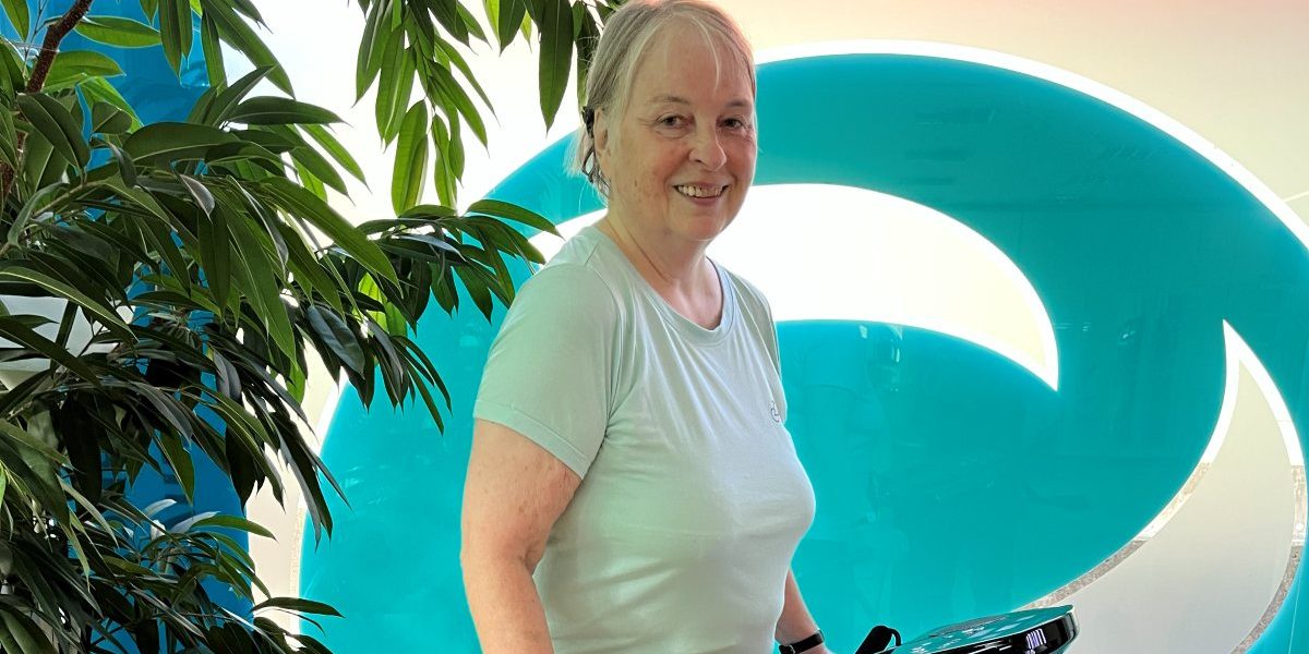 Vibrationstraining bei FEMISPORT: lächelnde Kundin an der Vibrationsplatte vor dem FEMISPORT-Logo in Neusäß